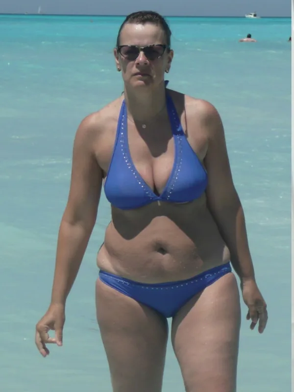 Femme en maillot de bain bleu debout dans l'eau claire d'une plage tropicale sous un soleil vif.